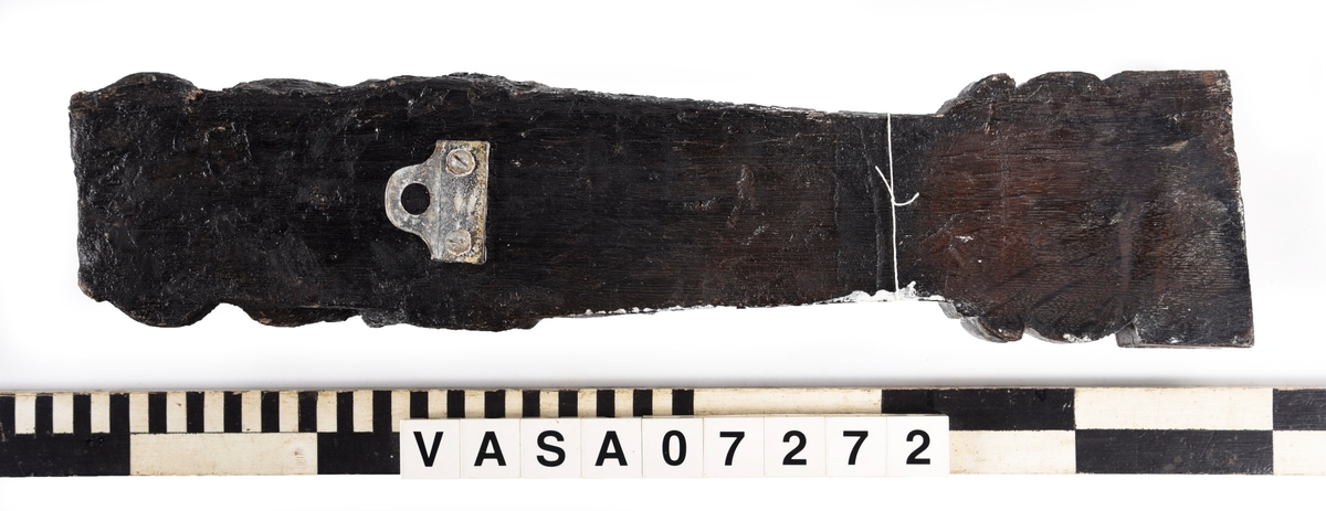 Liten skulpterad pilaster, utformad som en karyatid eller möjligen en putto. Figuren har långt hår och ett knubbigt ansikte, omgivet av en bred krage. Det nedåt avsmalnande pilasterskaftet är dekorerat med akantusblad. Nedtill avslutas pilastern av en rikt profilerad och dekorerad sockel. På skulpturens släta baksida sitter en nygjord upphängningsanordning, fästad med två skruvar.
Skulpturen är sliten.

Text in English: A small carved pilaster, with a caryatid or probably a putto. The figure has a chubby face, long hair and a broad collar. The lower part of the pilaster is decorated with acanthus leaves. The caryatid stands on a richly profiled and decorated socle. On the smooth back of the sculpture is a new hanging device attached with two screws.
The sculpture is worn.