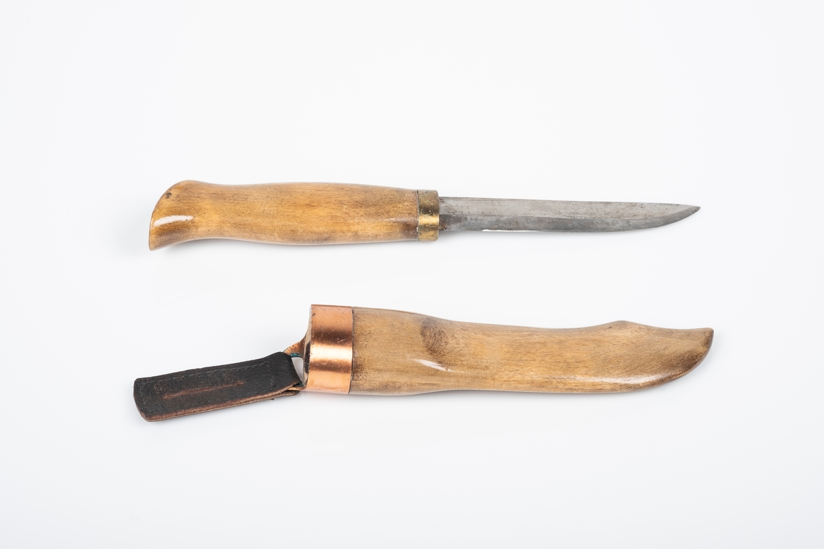 Håndlaget tollekniv med skaft og slire av tre, og knivblad av metall. Skaften og sliren er lakkert med blank lakk. Sliren er pyntet med kobberkant. Fra kobberkanten henger en svart skinnlapp med hull i til oppheng. Bolsteret er av messing.