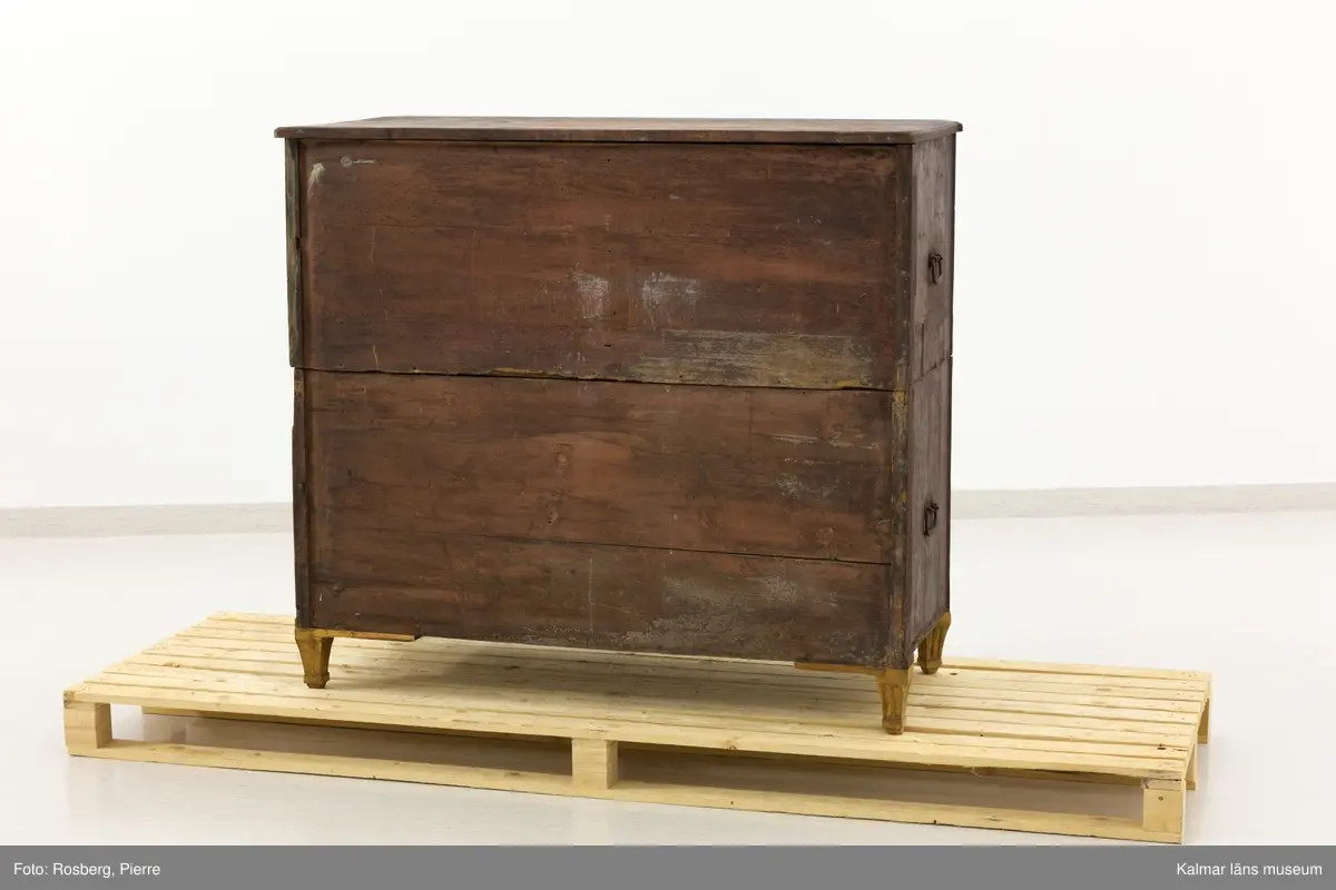 KLM 10747. Kista, dragkista. Av trä, furu, i sengustaviansk stil. Två stapelbara kistor med två lådor vardera istället för lock som på en vanlig kista. Varje del har handtag på kortsidorna så att de går att bära vid flytt. Som möbel fungerar den som en byrå. Räfflade, avskurna hörn och nedåt avsmalnande fötter, varav tre blivit utbytta till nya. Lådornas handtag är av mässing, de på kortsidorna av järn. Möbeln är ådringsmålad i en brun nyans, ej original. Undertill syns ett äldre färglager som går i en grå eller ljusblå nyans.