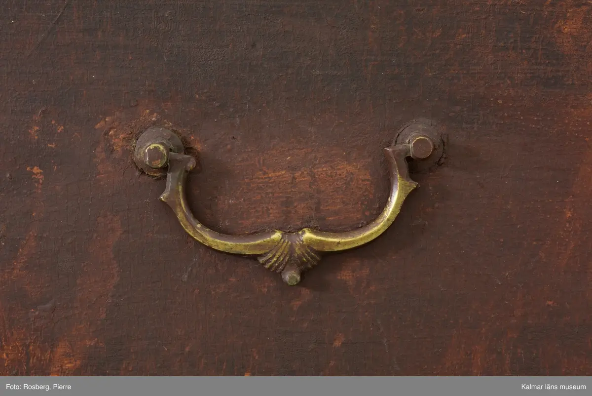 KLM 10747. Kista, dragkista. Av trä, furu, i sengustaviansk stil. Två stapelbara kistor med två lådor vardera istället för lock som på en vanlig kista. Varje del har handtag på kortsidorna så att de går att bära vid flytt. Som möbel fungerar den som en byrå. Räfflade, avskurna hörn och nedåt avsmalnande fötter, varav tre blivit utbytta till nya. Lådornas handtag är av mässing, de på kortsidorna av järn. Möbeln är ådringsmålad i en brun nyans, ej original. Undertill syns ett äldre färglager som går i en grå eller ljusblå nyans.