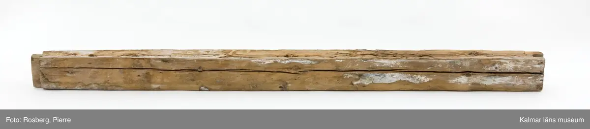 KLM 17275:4:1. Vägg, del av. En timmerstock tillhörande en innervägg. Hål för trädymlingar. På båda sidor bevarade fragment av bemålning, troligen från 1600-talet. På ena sidan måleri i bl.a. vitt och blått. På andra sidan bemålning i vitt, blått och grönt samt rester av påspikade tapeter. Även text skrivet med blyerts, något otydlig men troligen: Lundgren.