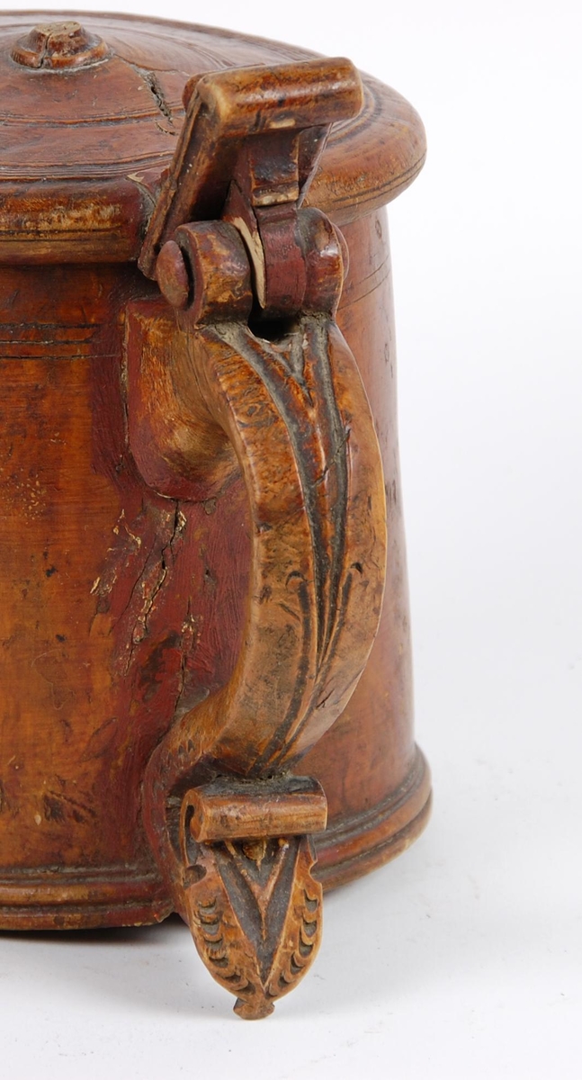 Kanne av dreid valbjørk. Lokket med dreide ringer. Bladformet lokkåpner. Hank med utskjæringer, ender i en spiss med bladdekor. Korpus med dreide ringformete bårder øverst,  fire målemerker innvendig.