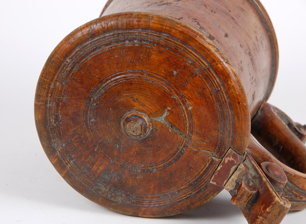 Kanne av dreid valbjørk. Lokket med dreide ringer. Bladformet lokkåpner. Hank med utskjæringer, ender i en spiss med bladdekor. Korpus med dreide ringformete bårder øverst,  fire målemerker innvendig.