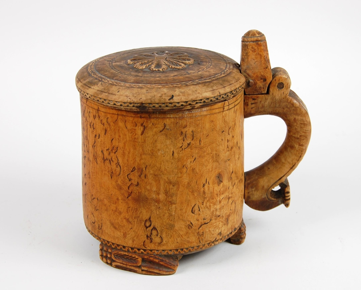 Kanne av dreid valbjørk. Lokk med skjært rosett og to bårder. Tre føtter med utskjæringer.