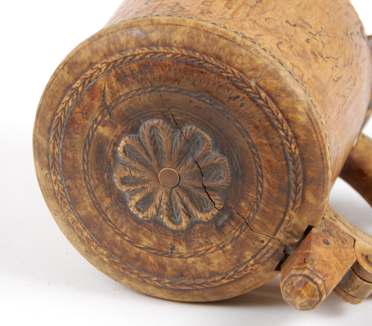 Kanne av dreid valbjørk. Lokk med skjært rosett og to bårder. Tre føtter med utskjæringer.