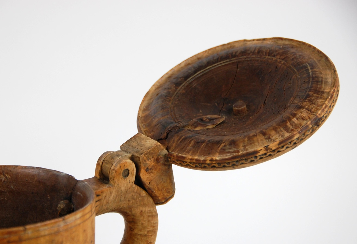 Kanne av dreid valbjørk. Lokk med skjært rosett og to bårder. Tre føtter med utskjæringer.