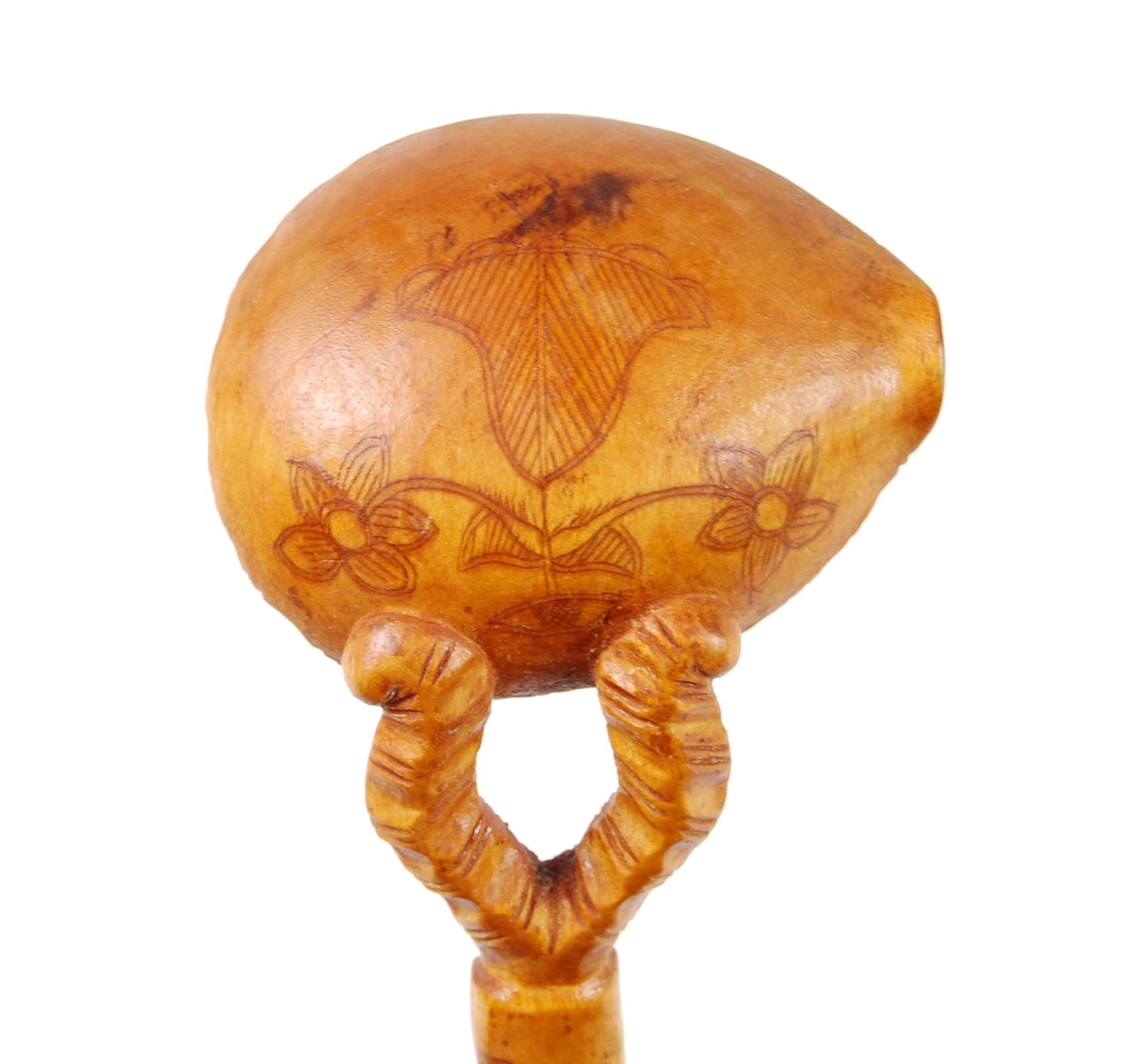 Skje av bjørk. Ovalt skjeblad med åpen tut på den enesiden, profilert langs kanten, kolrosingdekor på oversiden med bl.a. fuglemotiver og blomst, undersiden har kolrosingsdekor av blomster Halsen todelt. Skaftet har kolrosingdekor både på over- og undersiden, ender i en spiss.