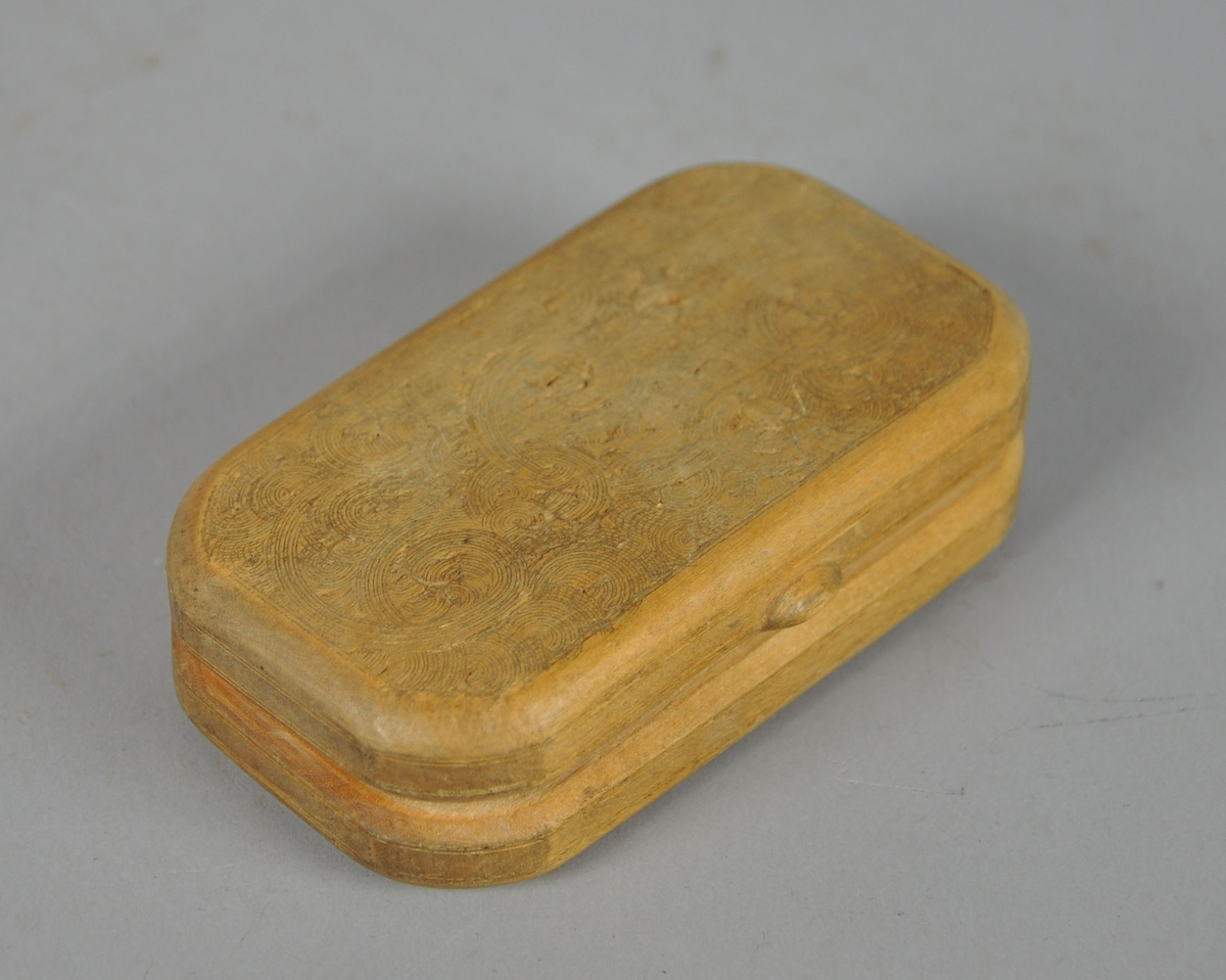 Rektangulær eske av tre, med avrundede kanter. På lokk og underside er det innrisset sirkulære streker. 

Dypere hakk enkelte steder i innrissingen kan tyde på at den dekorative treskjæringen er uferdig.