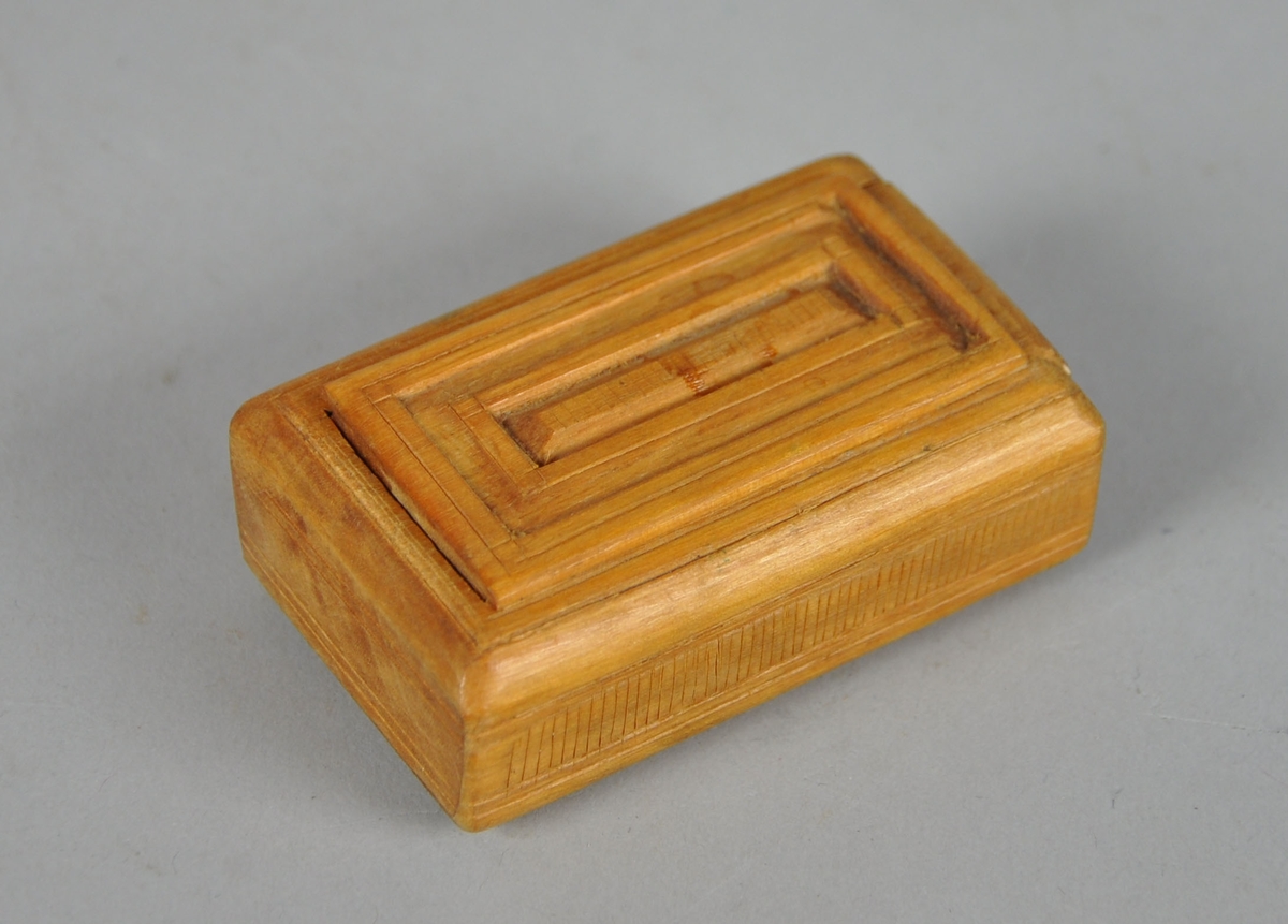 Eske av tre, med skyvelokk. Lokk og underside av eske er dekorativ utformet med treskjæring.