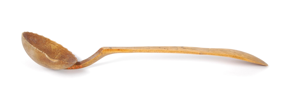 Skje av bjørk. Skjeblad tilnærmet sirkelformet, tungekant, kort nebb, kolrosingdekor på over- og underside hovedsakelig med blad- og blomstermotiver Buet hals. skaftet svakt bøyd nær enden, kolrosingdekor på over og underside med blad og blomstermotiver.