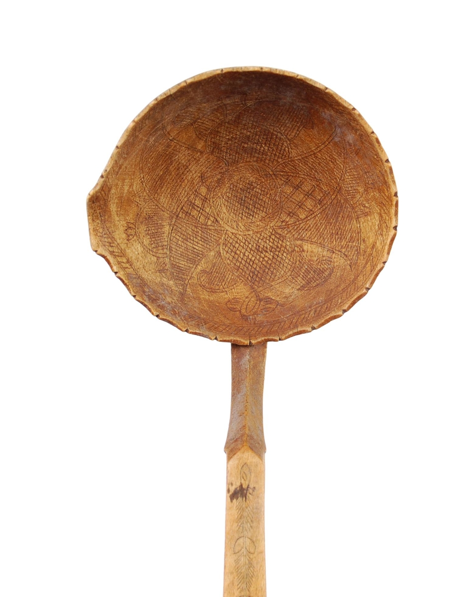 Skje av bjørk. Skjeblad tilnærmet sirkelformet, tungekant, kort nebb, kolrosingdekor på over- og underside hovedsakelig med blad- og blomstermotiver Buet hals. skaftet svakt bøyd nær enden, kolrosingdekor på over og underside med blad og blomstermotiver.