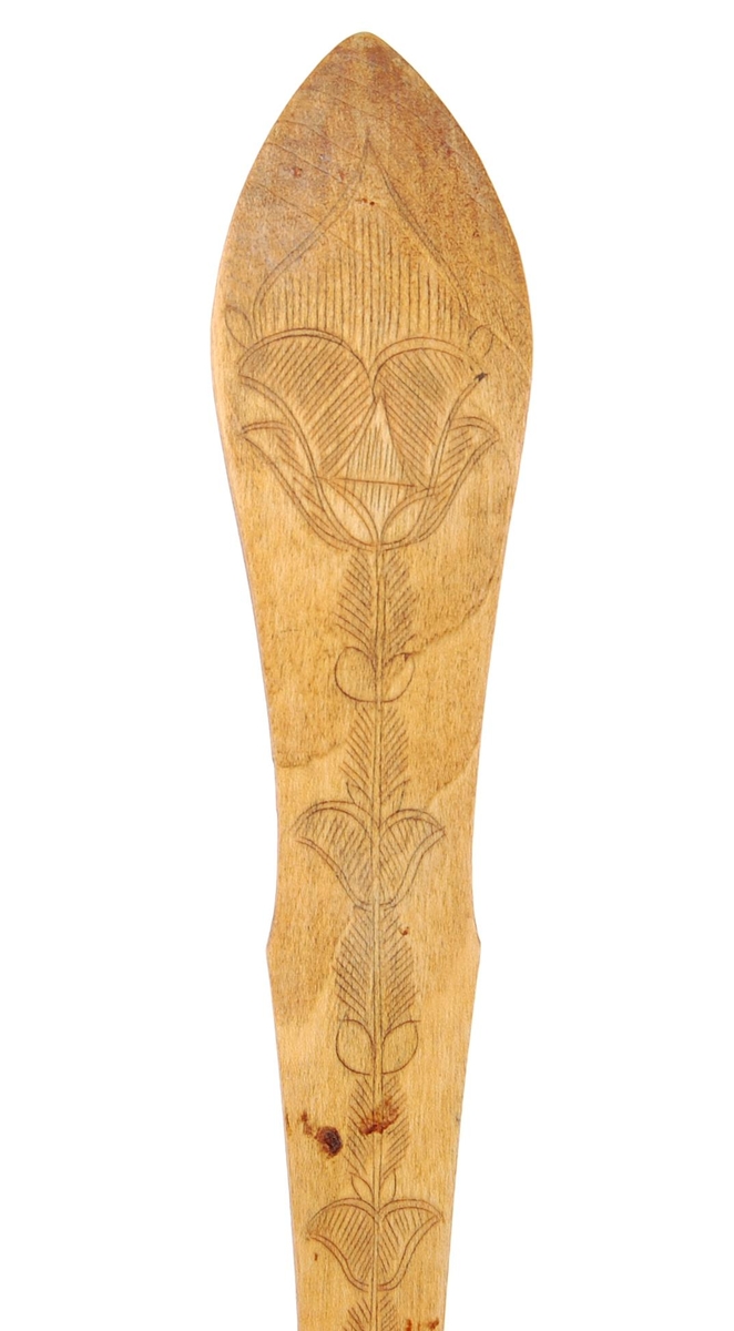 Skje av bjørk. Skjeblad tilnærmet sirkelformet, tungekant, kort nebb, kolrosingdekor på over- og underside hovedsakelig med blad- og blomstermotiver Buet hals. skaftet svakt bøyd nær enden, kolrosingdekor på over og underside med blad og blomstermotiver.