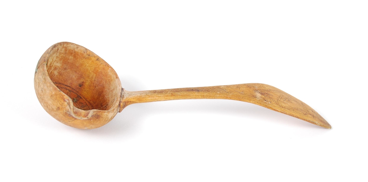 Skje av bjørk. Dypt skjeblad med nebb, i bunnen kolrosingdekor i form av bl.a. en stjerne, undersiden med kolrosingdekor i form av blader og blomster. Buet skaft med kolrosingdekor på over- og undersiden, undersiden har innskrift