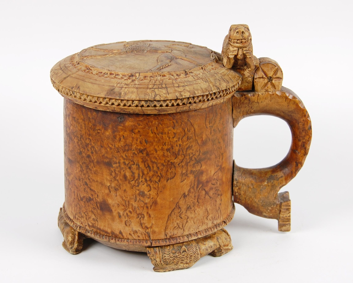 Kanne av dreid valbjørk. Lokket med uskåret springende løve omgitt av bård, bølgete utskjæringer langs kanten. Lokkåpner formet som en løve. Hanken med skjæringer langs kanten, ender i en spiss. Tre liggende løver danner føttene. Buemerke under.