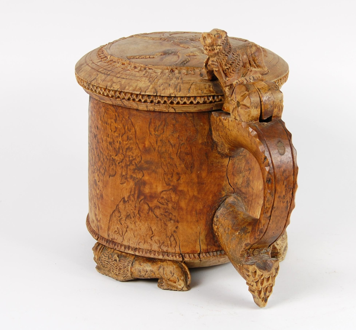 Kanne av dreid valbjørk. Lokket med uskåret springende løve omgitt av bård, bølgete utskjæringer langs kanten. Lokkåpner formet som en løve. Hanken med skjæringer langs kanten, ender i en spiss. Tre liggende løver danner føttene. Buemerke under.