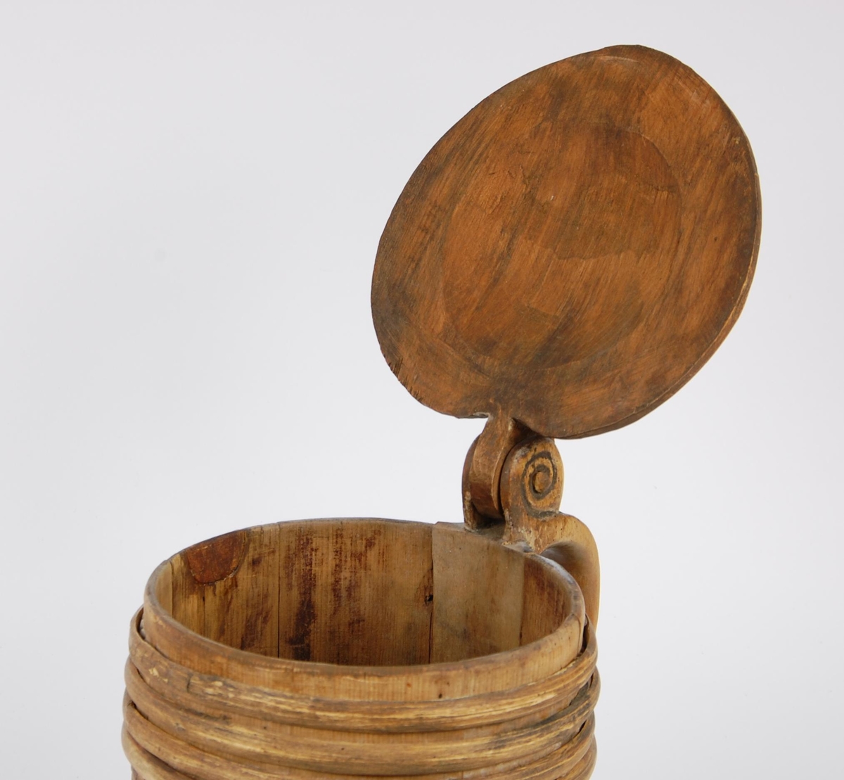 Kanne av trestaver. Lokket med bladlignende ranke, tungeformet bård langs kanten. Lokkgrepet er øverst kuleformet, nederst en ring  med skulpelignende utskjæringer. Hank med spiralformede utskjæringer oppe og nede, er i ett med en av stavene. Korpus har fire gjorder oppe og nede, mellom gjordene en akantusranke, like under og over gjordene tungeformede utskjæringer.