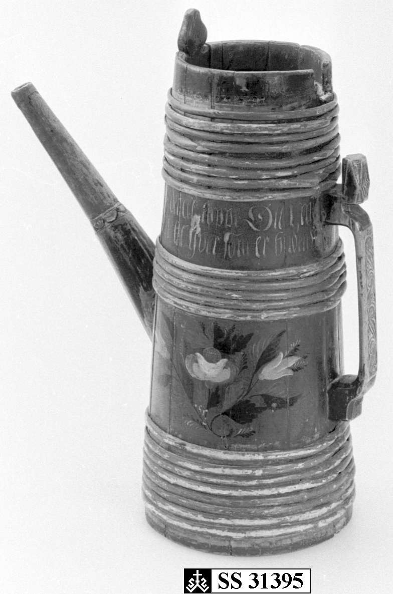 Kanne av furustaver. Fast lokk med rundt spunshull. Tuten er i ett med en av stavene som også er litt forlenget, tuten har jernbeslag ytterst. Hank er skåret ut av bakerste stav, er dekorert med akantusskurd. Korpus har åtte rødmalte gjorder øverst, fem rødmalte gjorder like over tuten og åtte rødmalte gjorder nederst, korpus dekorert med malte blad- og blomstermotiver. Lang inskrift