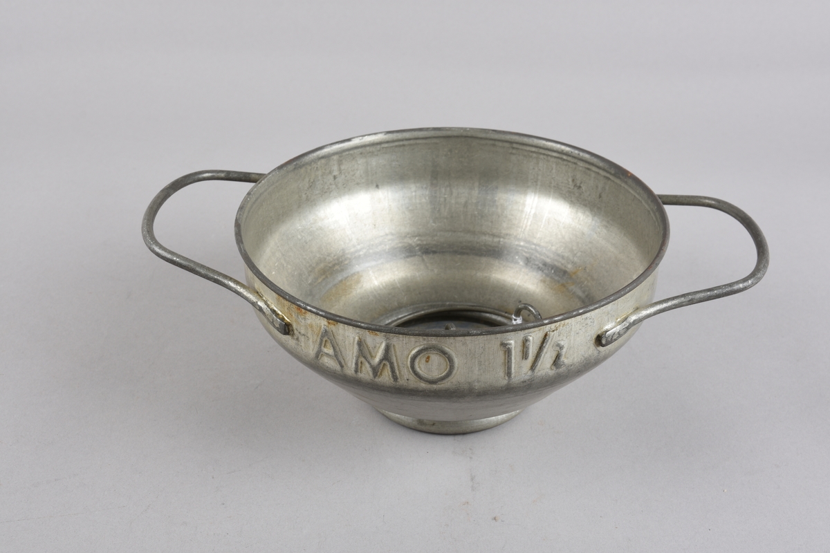 Rund mjølkesil med to hankar på sida. Munningsranden har falsa kant. Korpus skrår ujamnt nedover mot opninga i botn. Opninga har flat kant for plassering av silplate med festering. Det er to silplater med ulikt antal hol og ulik storleik på hola. Klemringen er av metalltråd, forma som ein ring med to oppbøygde endar som kan klemmast saman.