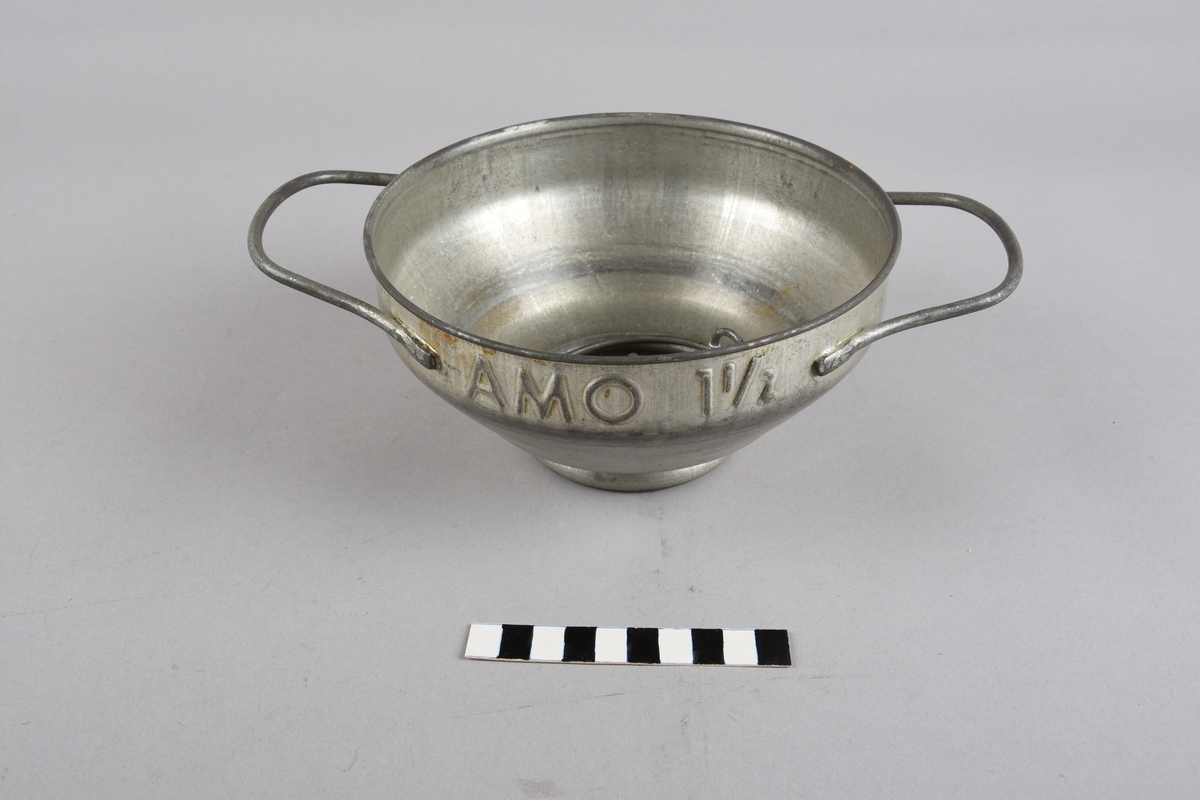 Rund mjølkesil med to hankar på sida. Munningsranden har falsa kant. Korpus skrår ujamnt nedover mot opninga i botn. Opninga har flat kant for plassering av silplate med festering. Det er to silplater med ulikt antal hol og ulik storleik på hola. Klemringen er av metalltråd, forma som ein ring med to oppbøygde endar som kan klemmast saman.