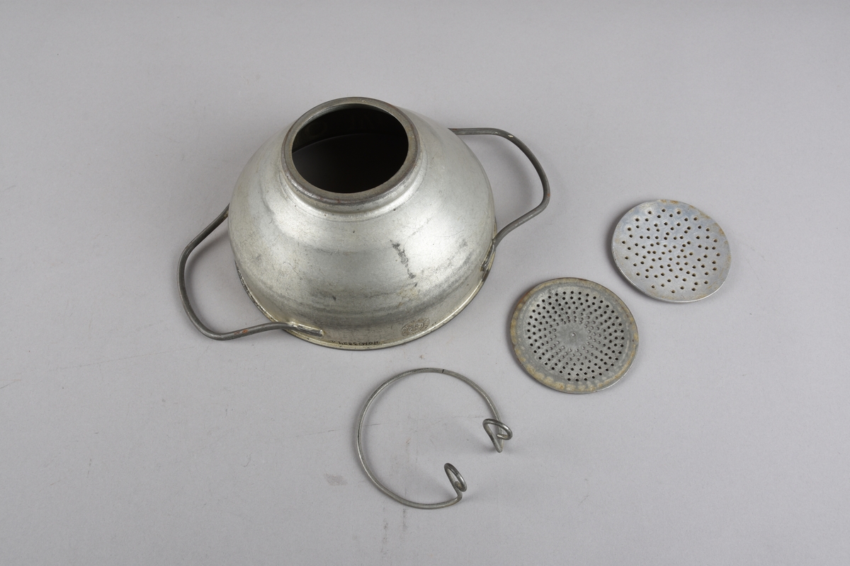 Rund mjølkesil med to hankar på sida. Munningsranden har falsa kant. Korpus skrår ujamnt nedover mot opninga i botn. Opninga har flat kant for plassering av silplate med festering. Det er to silplater med ulikt antal hol og ulik storleik på hola. Klemringen er av metalltråd, forma som ein ring med to oppbøygde endar som kan klemmast saman.