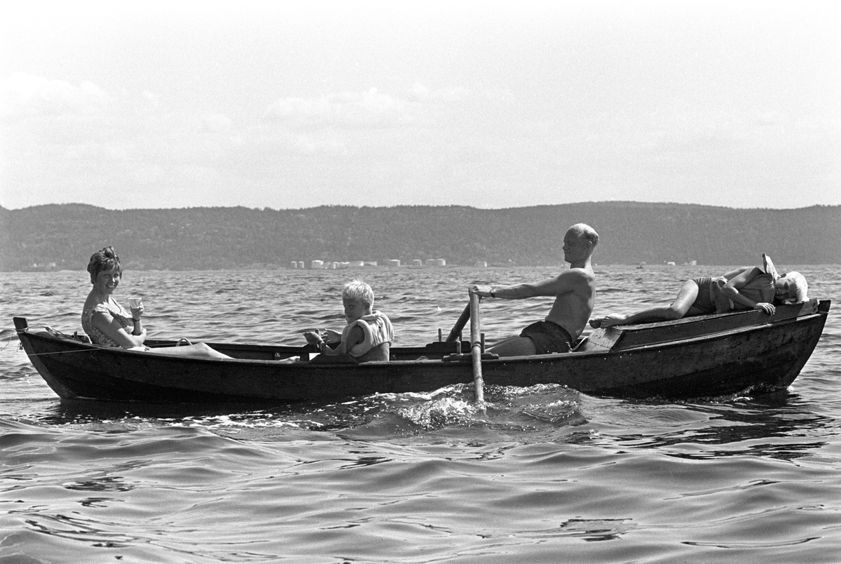 Erik Damman, reklamekonsulent fra Oslo, ferierer i båt med familien i Oslofjorden. De skal ro 10 - 12 mil i løpet av 8 - 10 dager, og går i land på små holmer som fjorden har mange av. Her sitter Erik Damman ved årene. Ragnhild Damman til venstre. Midt i båten Are (8), Brede (5) og Rein (10) helt forut.