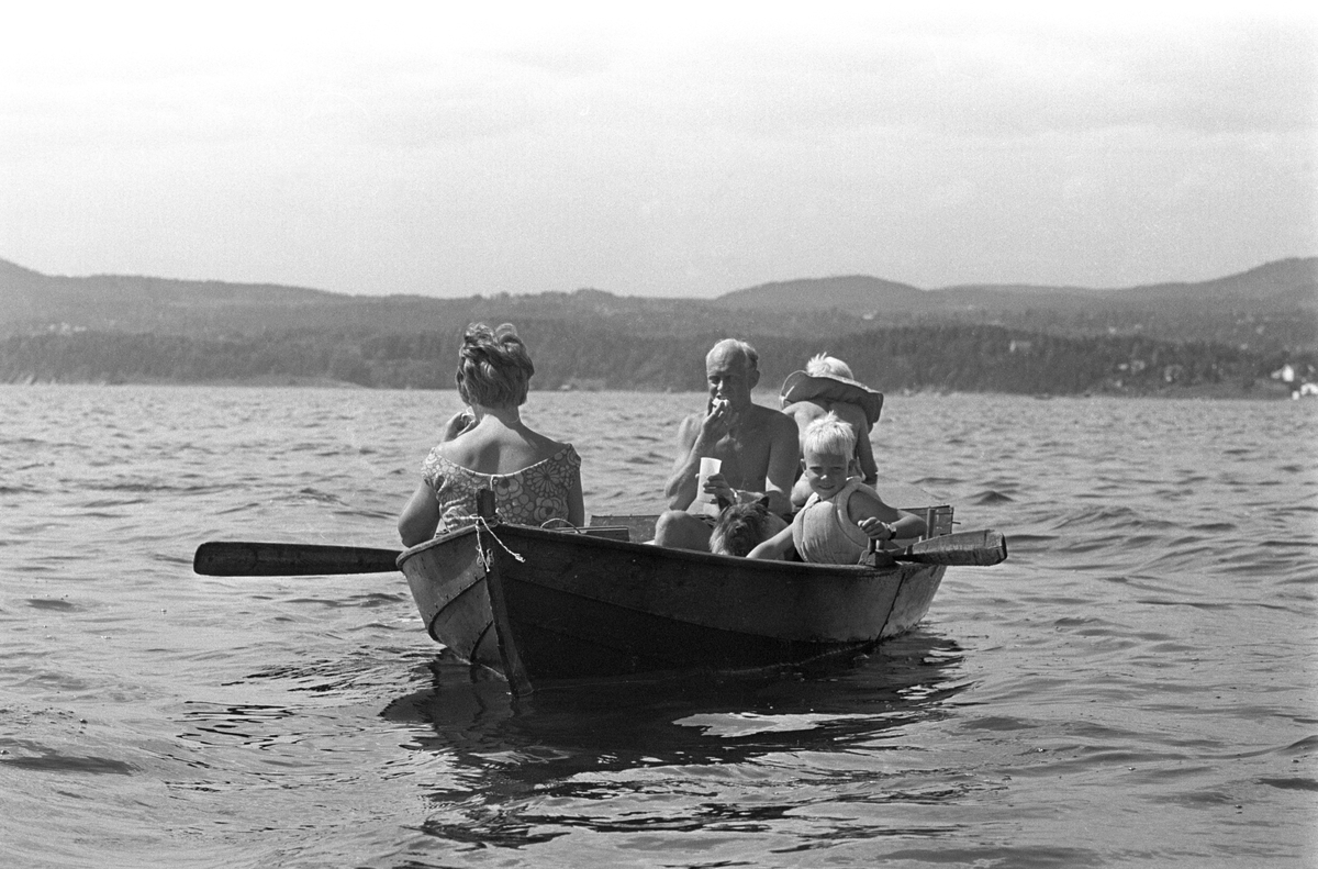 Erik Damman, reklamekonsulent fra Oslo, ferierer i båt med familien i Oslofjorden. De skal ro 10 - 12 mil i løpet av 8 - 10 dager, og går i land på små holmer som fjorden har mange av. Her sitter Erik Damman ved årene. Ragnhild Damman med ryggen til. Midt i båten Brede (5), Are (8) og hunden Rocky. Rein (10) helt forut.