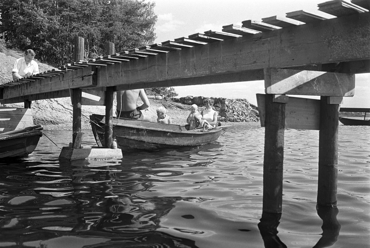 Erik Damman, reklamekonsulent fra Oslo, ferierer i båt med familien i Oslofjorden. De skal ro 10 - 12 mil i løpet av 8 - 10 dager, og går i land på små holmer som fjorden har mange av. Like før avreise fra Brønnøya. Ragnhild Damman i båten med Jaran (1,5). I midten Are (8) og Brede (5). Erik Damman med ryggen til.