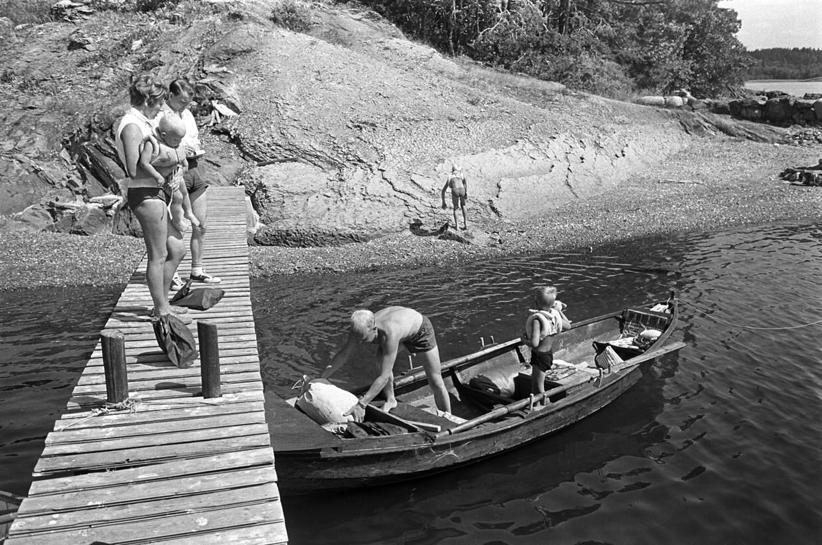 Erik Damman, reklamekonsulent fra Oslo, ferierer i båt med familien i Oslofjorden. De skal ro 10 - 12 mil i løpet av 8 - 10 dager, og går i land på små holmer som fjorden har mange av. Like før avreise fra Brønnøya. Ragnhild Damman på brygga med Jaran (1,5). I båten Erik Damman og Brede (5).