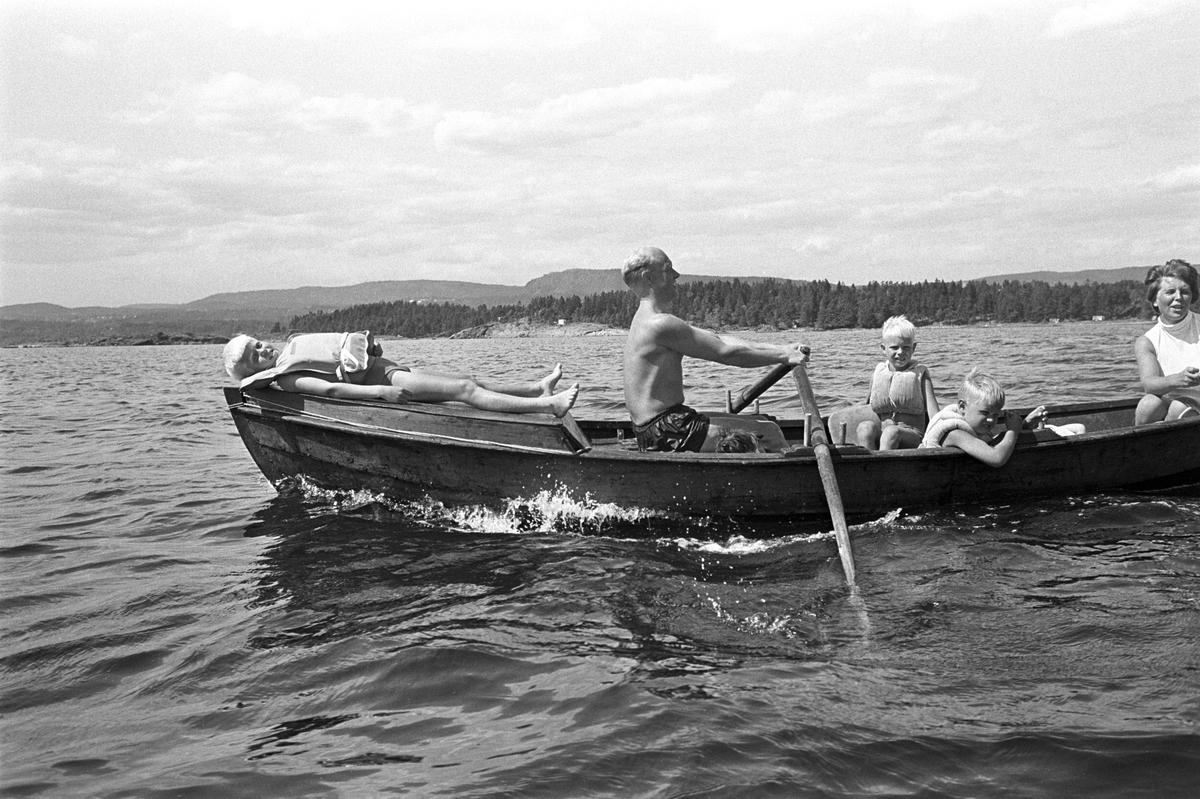 Erik Damman, reklamekonsulent fra Oslo, ferierer i båt med familien i Oslofjorden. De skal ro 10 - 12 mil i løpet av 8 - 10 dager, og går i land på små holmer som fjorden har mange av. Erik Damman ved årene. Ragnhild Damman sammen med Are (8) og Brede (5). Rein (10) ligger på soldekket forut.