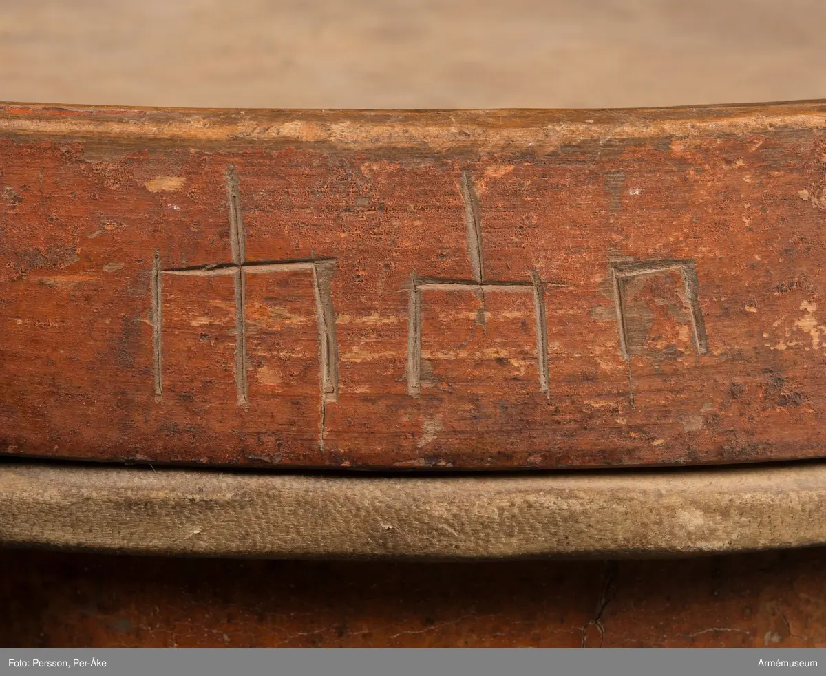 Cylindertrumma av trä med bemålad lim och krita grunderad duk.
Ytan är krackelerad med ett visst bortfall, dock relativt stabil. Tre hål i varierande storlek.

Membran: övre skinnet är smutsigt och repigt med tendenser till sprickbildning. Det finns en centimeterstor lagning. Det undre, har en tvärsgående spricka som tudelar skinnet. Den större delen rullar in mot mitten. Det finns fläckar av ngn. lättlöslig, gråaktig lösning. 

Veckelgjordar: har lindade fogar, den övre med tunt rep/lina, 
Den undre med rep och smalt läderband. Tre tecken inskurna i övre veckelgjordens utsida, som liknar: 1:a,  gaffel med tre klor, 2:a, endast de två yttre klorna och skaft, 3:e tecknet: endast de två yttre klorna, skaftet saknas. 

Spännlina: är fin med tvinnat, avsmalnande repslut. Det finns åtta spännstroppar varav två stycken är fransade.

Spännringar : Utsmyckning : röda kilar målade på gul botten. Mönstret ristat i grunden.

Märkning: fastklistrad Konung Karl den XII med ifyllnad: Litt B  No.4 
Hängandes pappers etikett  i påse No 1211,
Gustavianska koret No 9.