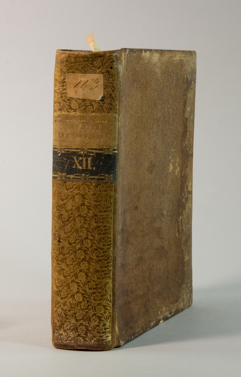 Bok, helfranskt band "Descriptions des arts et métiers" ny upplaga, vol. XII, med planscher, utgiven av J.E. Bertrand och tryckt i Neuchatel 1780.  
Bandet med blindpressad och guldornerad rygg, titelfält med blindpressad titel och ett mörkare fält med volymens nummer. Pärmens insida klädd med marmorerat papper. Med rött snitt.
Påklistrad etikett märkt med bläck "No 3."