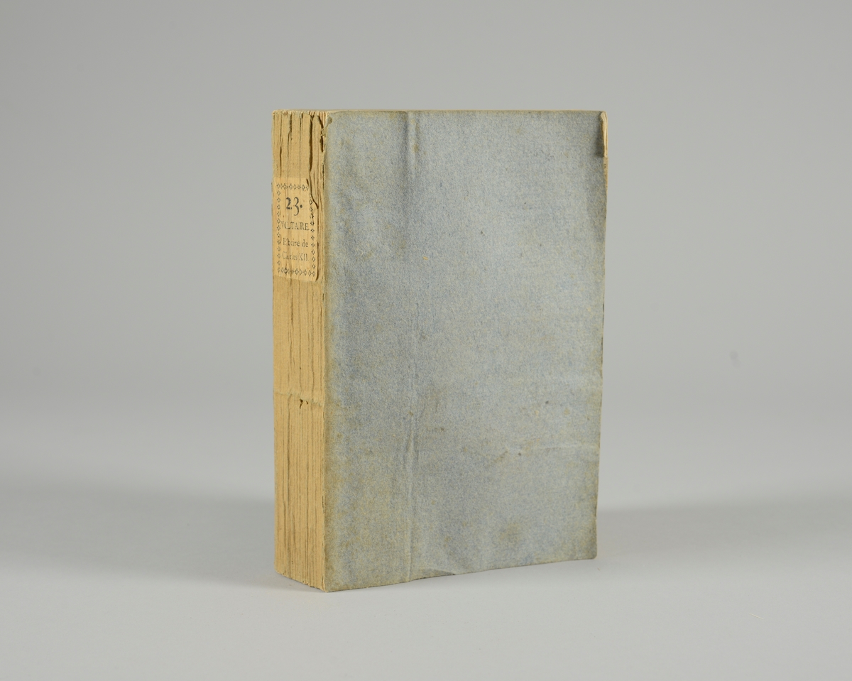 Bok, pappband,"Oeuvres completes de Voltaire", del 23 Histoire de Charles XII, tryckt 1785.
Pärmen klädd med gråblått papper, på pärmens baksida klistrad sida ur annan bok. Med skurna snitt. På ryggen klistrad pappersetikett med tryckt text samt volymens nummer. Ryggen blekt.