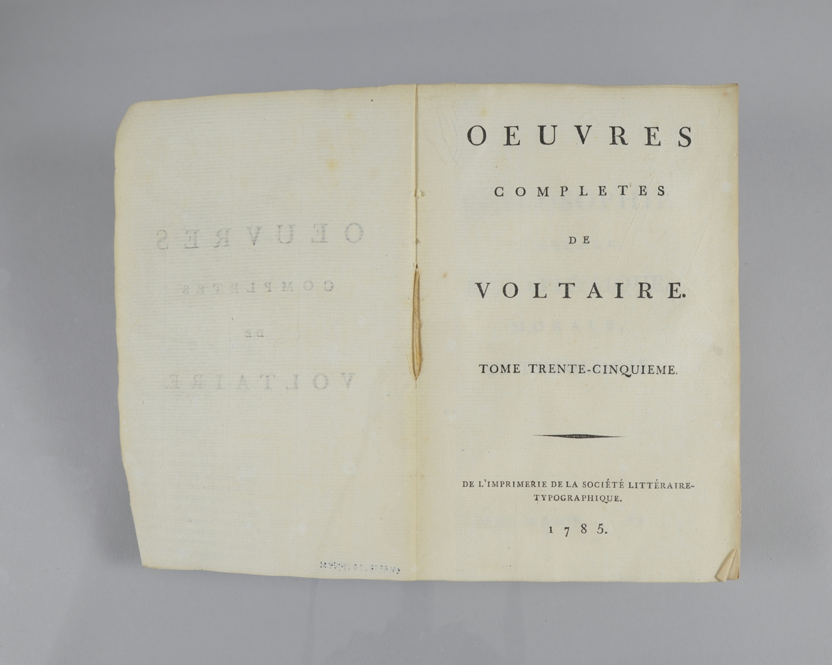 Bok, pappband,"Oeuvres completes de Voltaire", del 35, tryckt1785.
Pärmen klädd med gråblått papper, på pärmarnas insidor klistrade sidor ur annan bok. Med skurna snitt. På ryggen klistrad pappersetikett med tryckt text samt volymens nummer. Ryggen blekt.