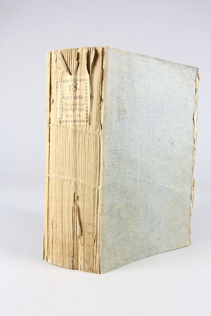 Bok, pappband,"Oeuvres complètes de Voltaire." del 38, tryckt 1785.
Pärm av gråblått papper, på pärmens insidor klistrade sidor ur annan bok, skurna snitt. På ryggen pappersetikett med tryckt text med volymens namn och nummer. Ryggen blekt.