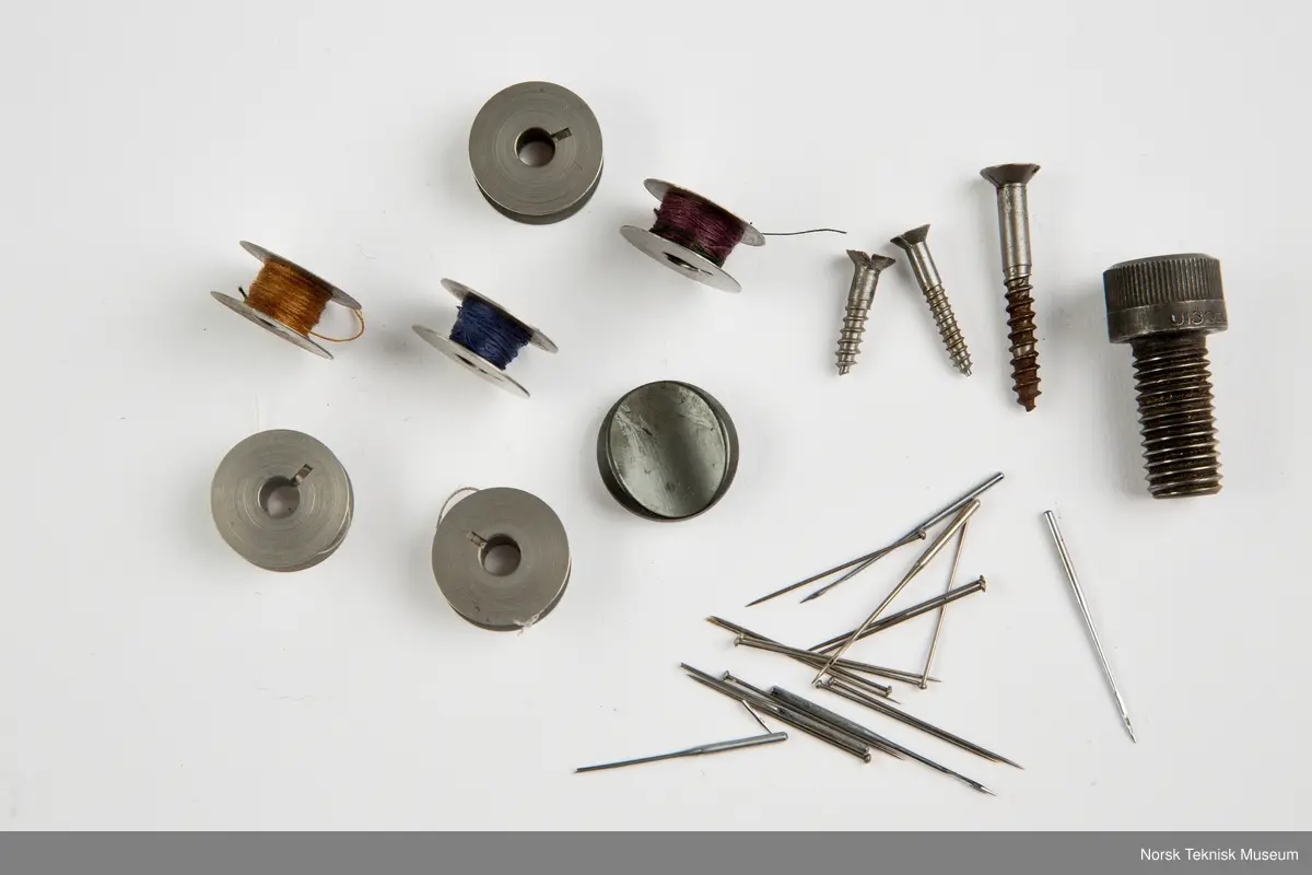 Lokket mangler. Inneholder oljekanne, verktøy, nåler, spoler, rem, symaskinfot, trådsnelle.