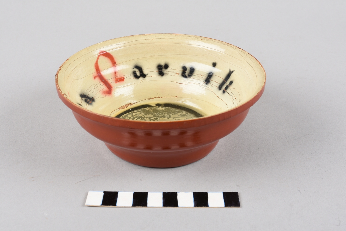 Dreid treskål med dekor på innsida, Flat botn, bølgeforma sider. Inni skåla er det tekst, i botn pålimt fotografi, truleg over Ofotfjorden med Veggfjellet i bakgrunnen. Lakka over fotografiet. Reiseminne