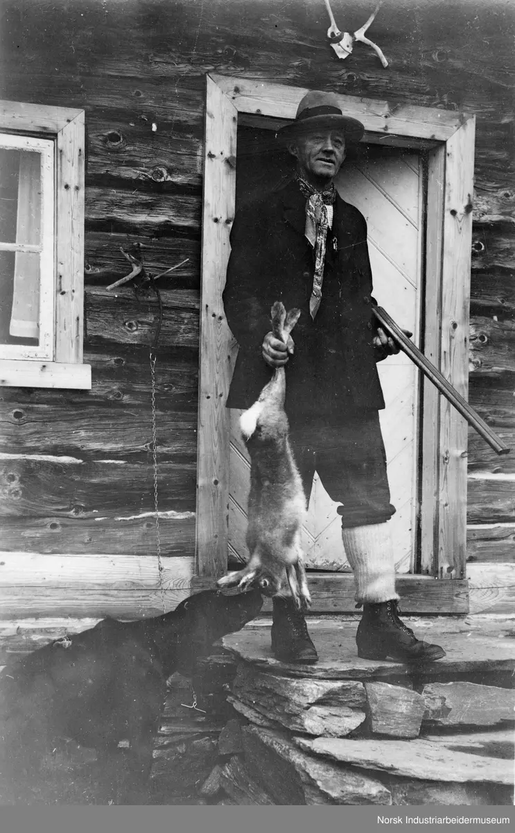 En jeger viser frem en hare. En hund snuser på byttet.