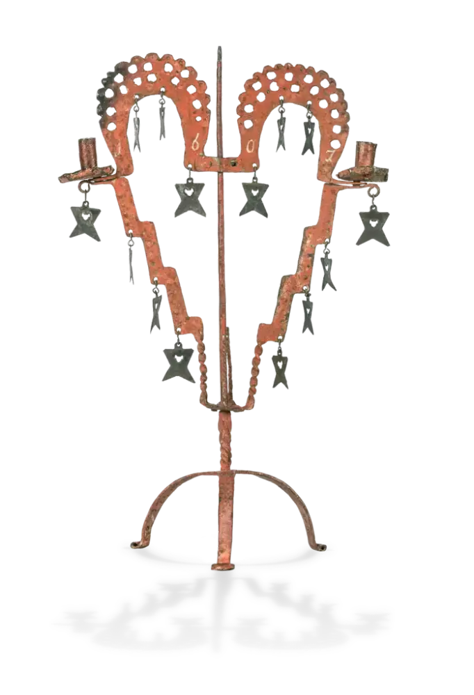 Bildet viser en lysestake fra 1607. Lysestaken er oransje og formet som et hjerte. På den henger det forskjellige symboler. Det er plass til to lys i den.