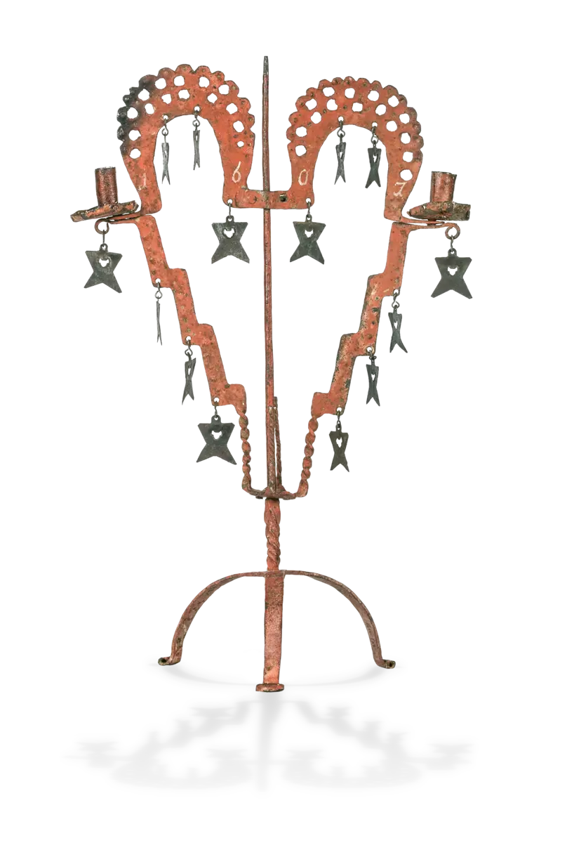 Bildet viser en lysestake fra 1607. Lysestaken er oransje og formet som et hjerte. På den henger det forskjellige symboler. Det er plass til to lys i den.