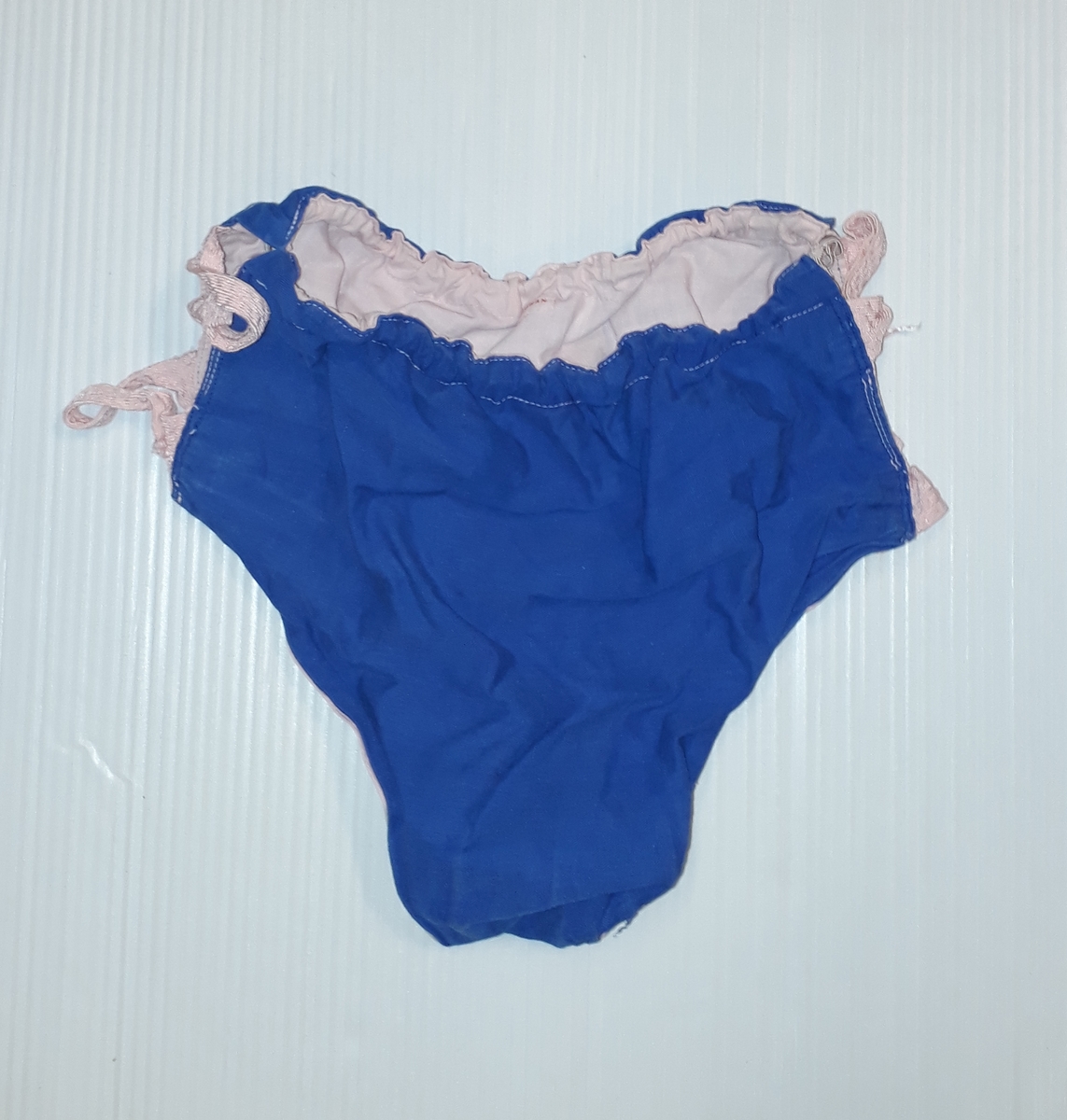 Blommig säck av galontyg innehållande badkläder: rutig bikini, blå badbyxor och blå/rosa bikinibyxor. Medföljde vid insamlingen av Vegkryssaren TERTIA.