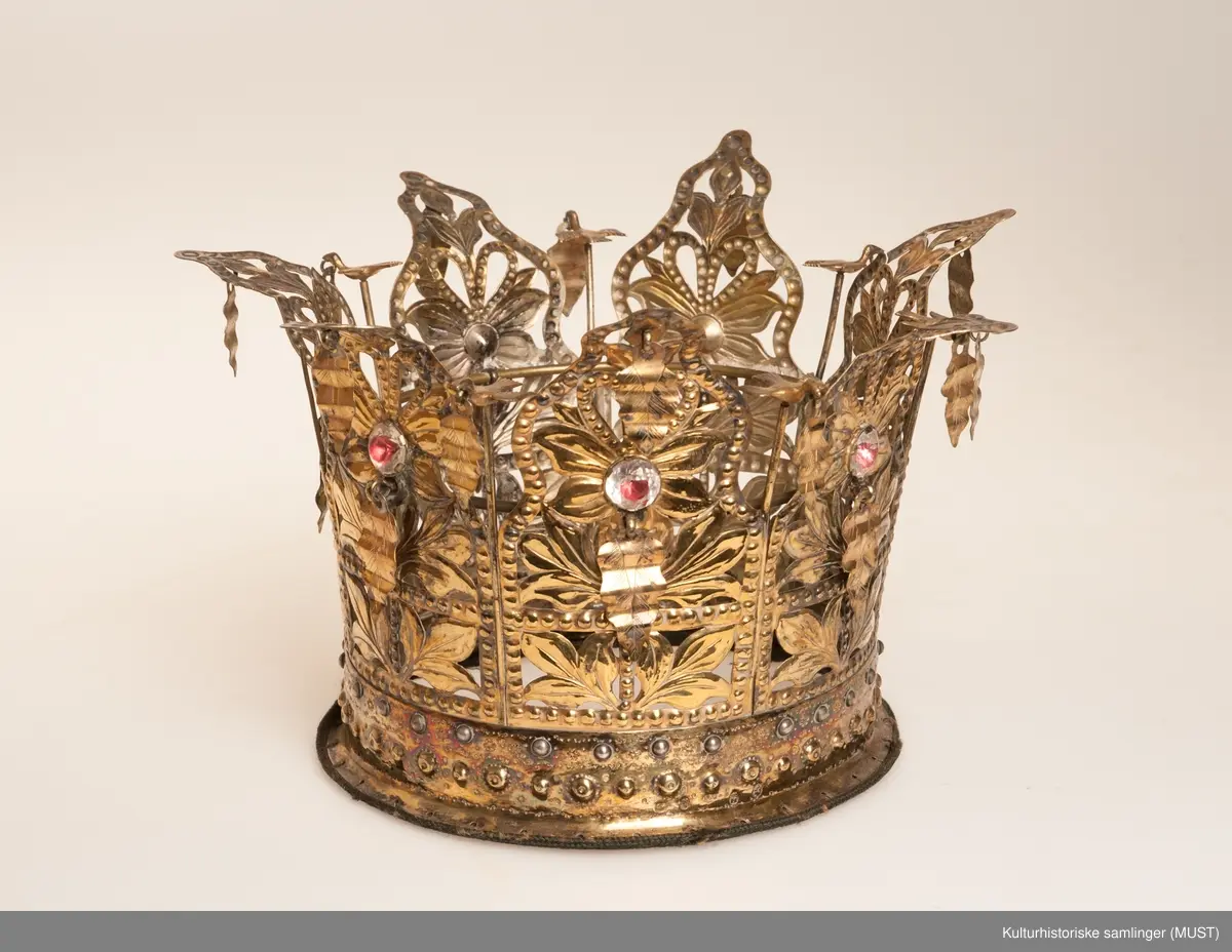 Brudekrone i forgylt sølv. Presset arbeide. Forholdsvis bred bærering med to rader små bukler og ornamentlinjer slått inn med med blad - og blomstformede punsler. Til bæreringens overkant er fastklinket sju gjennombrutte takkestykker som er sammenhengslet. Mønsteret i hvert takkestykke består av en blomst med blader og en foliert glassten. Over blomsten et hjerte, dessuten er til hver takke festet to riflede løv. Mellom takkene står en fugl med utbredte vinger og et løv i nebbet. Stemplet på utsiden av bæreringen med Bergens bymerke og Hoffs guardeinmerke ( stempelmerke fra offentlig ansatt mann som på forlangende skulle prøve finheten av edle metaller ). 