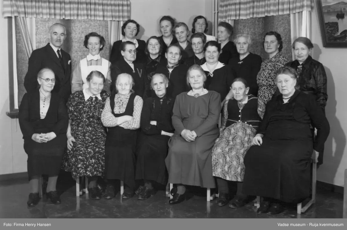 Gamlehjemsforeningen i Vadsø. Første rekke fra v.Thekla Olsen, Hanna Pedersen, Jensine Zahl, fru Arvid Johansen, Heville Pedersen, ukjent, Else Trælstad. 2.rekke fra v.: Ukjent mann, bestyrer Ella Walle, Emilie Henriksen, Anny Arne Pedersen, ukjent, Valla (Henry) Hansen, fru Løfgren, Karoline Rollstad, Karlida Langseth, ukjent, Buck Henriksen. Bakerste rekke: Mimmi Junge, Bergitte Saxi, Caroline Lebesby, Martha Mathinahå, Johanne ELine Hoel