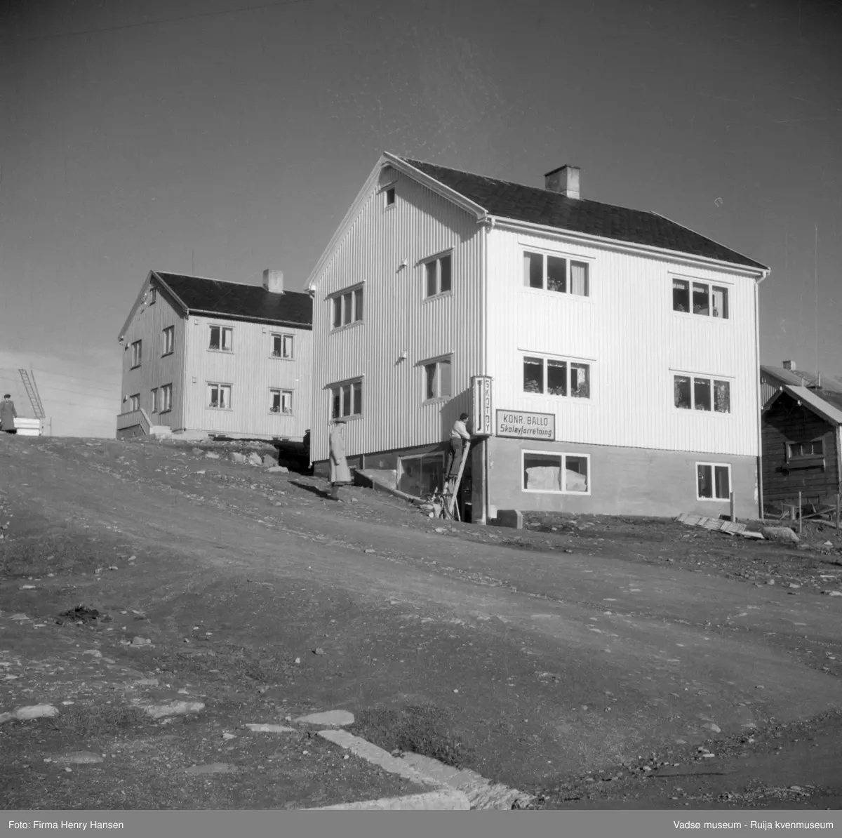 Vadsø, Bildet tatt fra Nyborgveien mot nordøst. Gata midt i bildet er Evangers gate, som fører opp til Damsveien.. Huset midt i bildet er et gjenreisingshus i 2 etasjer med Konr Ballos skotøyforretning i  kjelleretasjen.