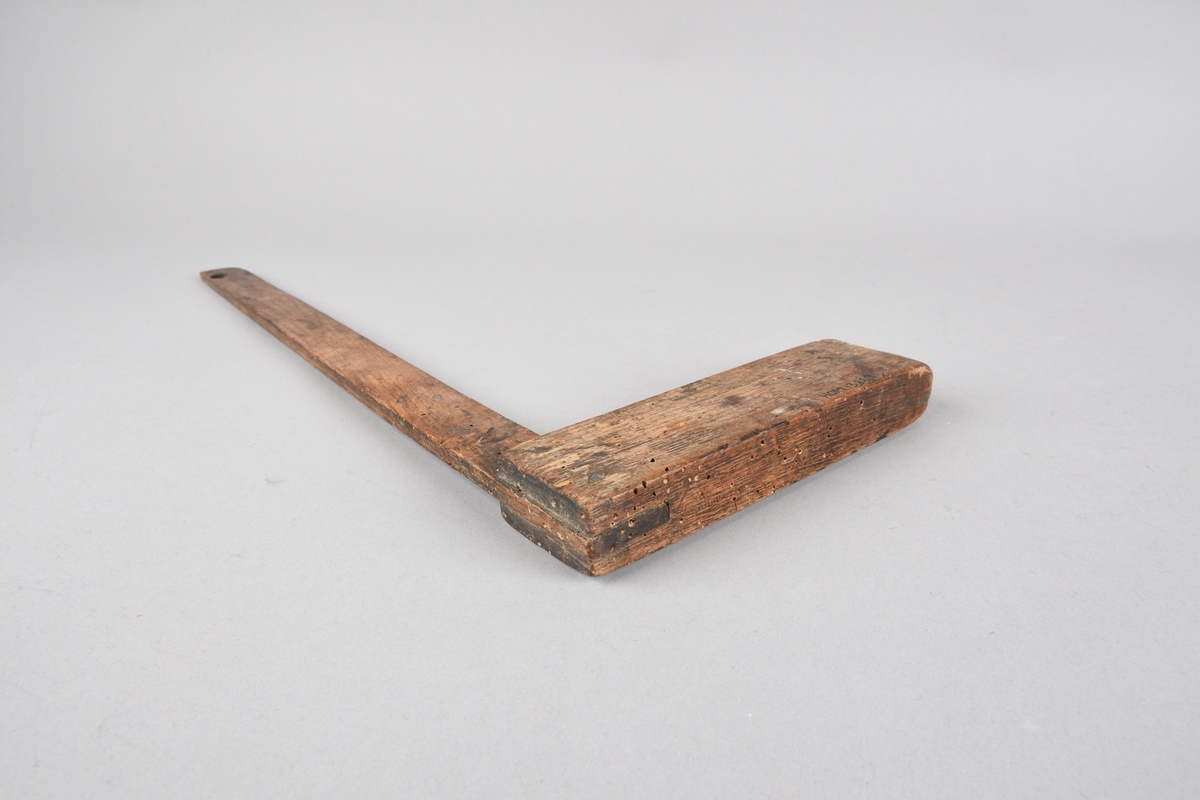 Vinkel til snikkararbeid, 90 gradar. Han er slissa saman av to vinkelarmar av tre, med tre gjennomgåande trepluggar til feste. Den kortaste armen er kraftigare enn den lange, og er avrunda i ytste enden . Ytste ende av den lange armen har eit hol samt ein tilskoren profilmal i eine hjørnet.