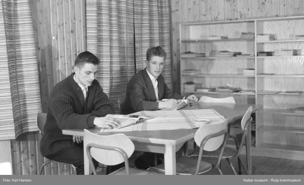Finnmark Landbruksskole, Tana. 2 menn i lesesalen/biblioteket.
Skolen gikk først under navnet Fagskolen for Finnmarkens næringsliv.  I 1923 ble navnet endret til Finnmark landbruksskole. I førkrigsårene var det hektisk aktivitet ved skolen, det ble bl.a. reist et nytt internat i 1938. I august 1940 overtok tyskerne. All undervisning ved skolen ble innstillt og høsten 1944 ble bebyggelsen i Tana brent. Først i 1956 var gjenreisningen kommet så langt at det første kullet etter krigen kunne begynne. I 1958 ble arbeidet med det nye undervisningsbygget igangsatt. Inntil dette stod ferdig i 1960, måtte undervisningen foregå i internatbygningen. (www.nsd.uib.no)