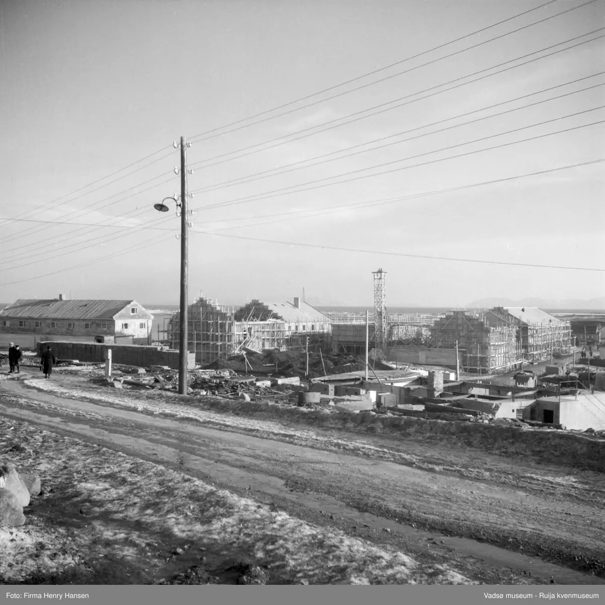 Vadsø sentrum. Gjenreisninga av Sentrum i full gang. Forretningsbyggene rundt Torget, øst for Tollbugata ; bla  Rolf Hansen, Henry Hansen og Baker Henriksen under oppføring. Vi ser også forretningsbygget til Leif Bjerck. Bildet er tatt fra Nyborgveien mot sydøst. .