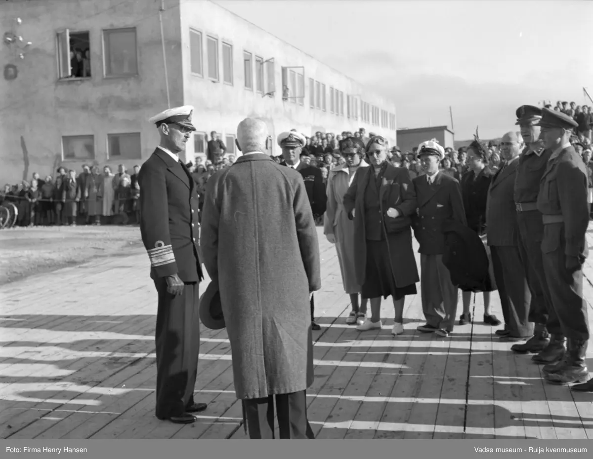 Vadsø. Kongebesøk i Vadsø 1950. Kongen og kronprinsfamilien blir tatt imot på kaia. Vi ser kong Haakon, kronprins Olav, prinsesse Astrid, kronprinsesse Märtha og prins Harald. Havnebygget i bakgrunnen.
Kong Haakon og kronprinsfamilien besøkte Vadsø 25.-26.7.1950 i forbindelse med en større rundreise i Nord-Norge sommeren 1950. Under besøket sto "biltur gjennom byen" og "besøk på sykehuset" på programmet. Kilde: Det kongelige hoff, arkivet