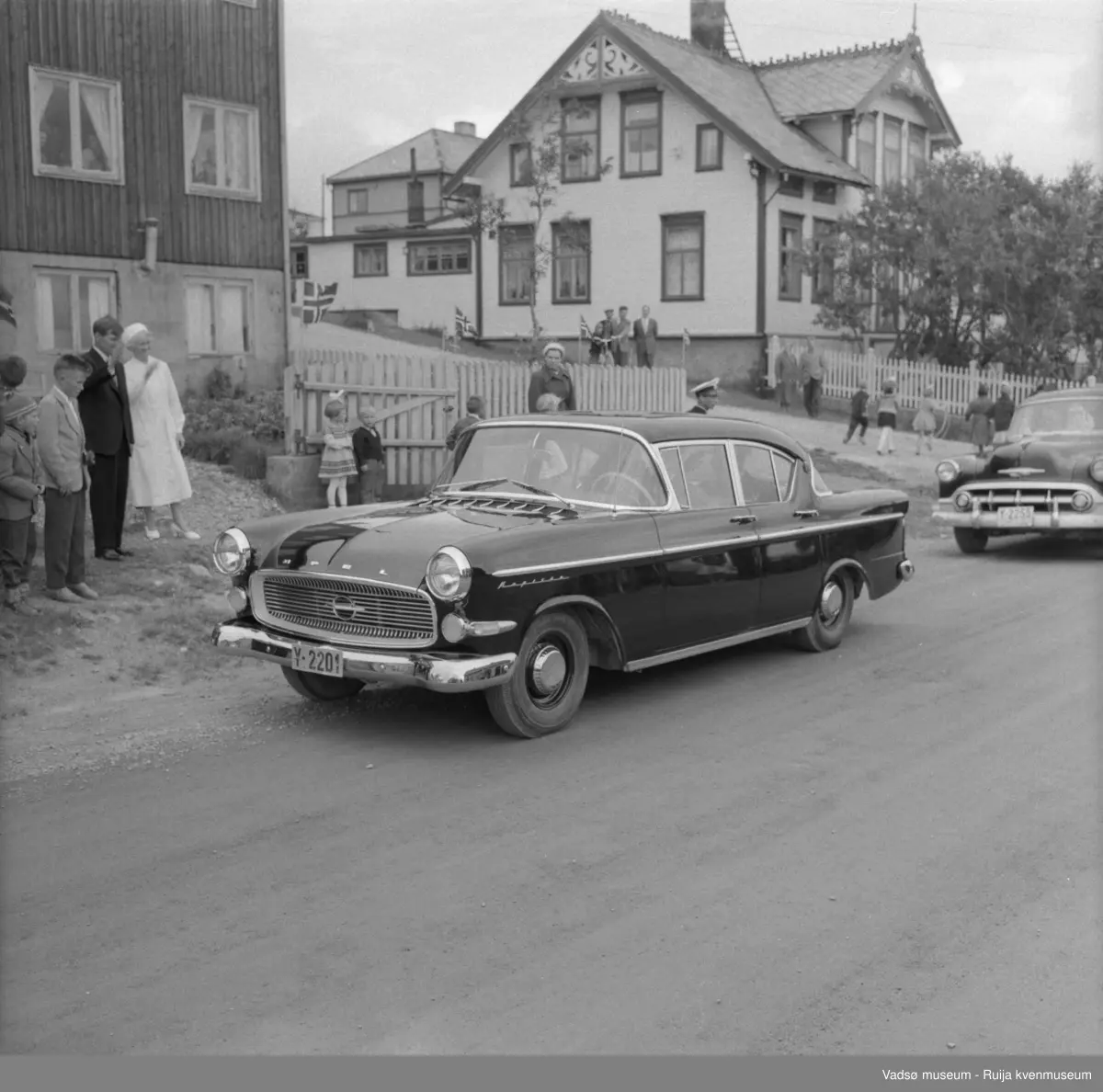 Vadsø juli 1959. Kongebesøk. Bil Y-2201 står parkert i Nyborgveien, ved Alders hvile, drosje Y-2255 parkert bak. Andreas Esbensens hus til høyre.