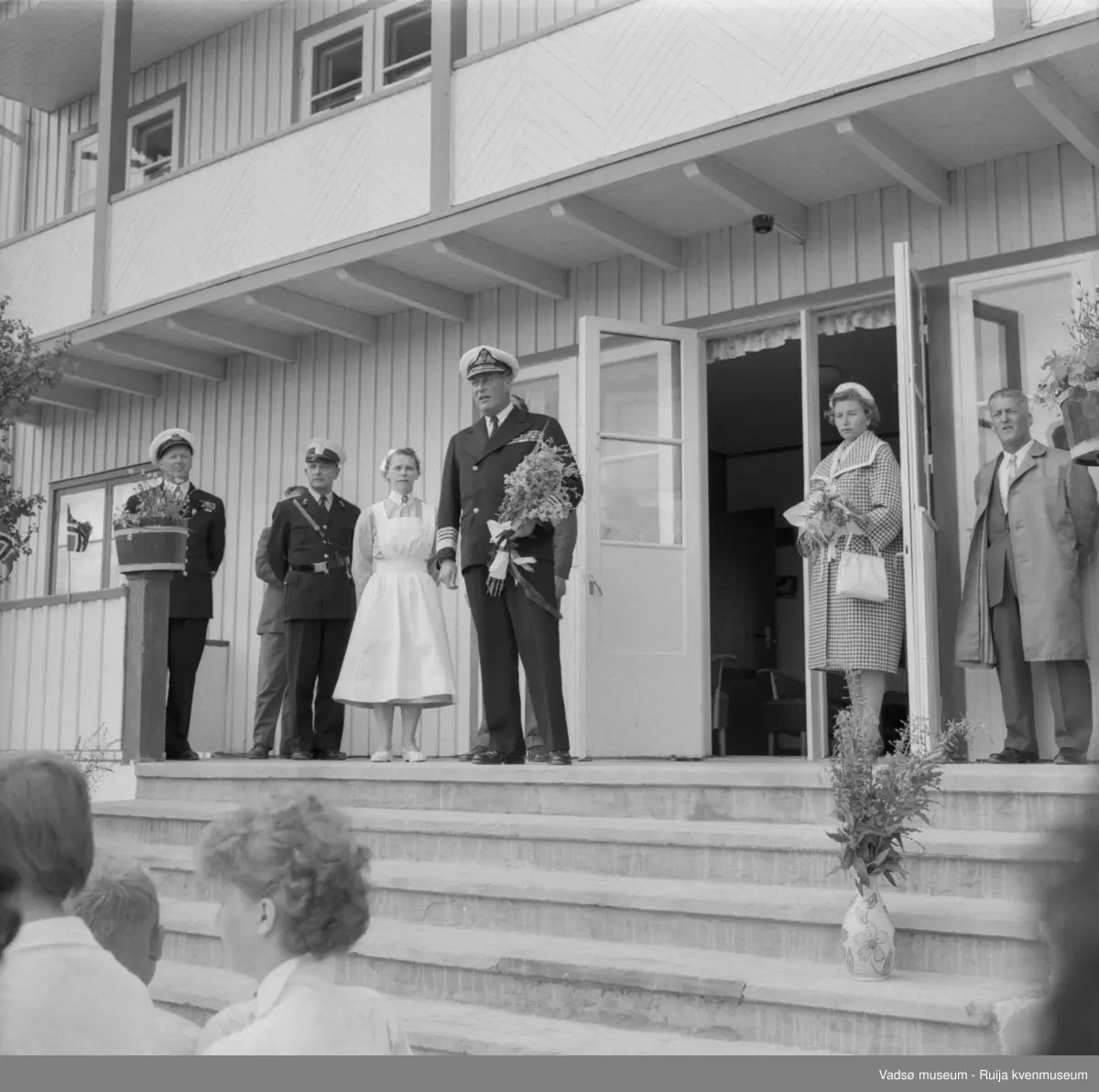 Vestre Jakobselv juli 1959. Kongen på trappa til barnehjemmet Vårsol. Til venstre for kongen, bestyrerinnen søster Gunvor. Til høyre for kongen prinsesse Astrid og fylkesmann Peder holt.