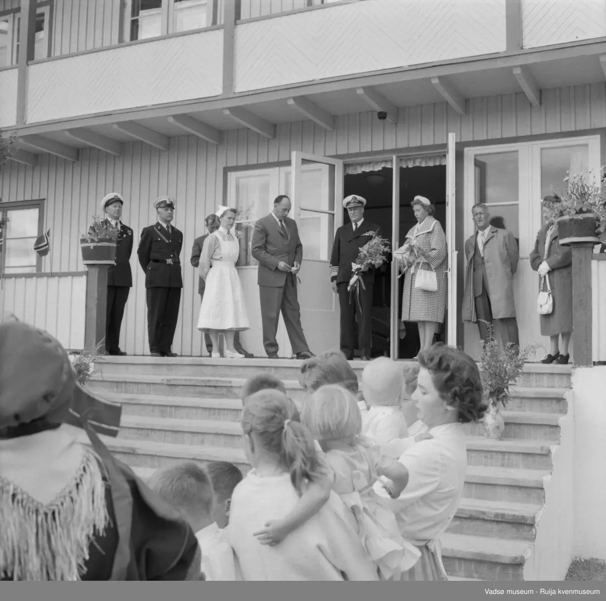 Vestre Jakobselv juli 1959. Kongen på trappa til barnehjemmet Vårsol. Til venstre for kongen, bestyrerinnen søster Gunvor og ordfører i Nord-Varanger, Henry Karlsen. Til høyre for kongen prinsesse Astrid og fylkesmann Peder Holt.